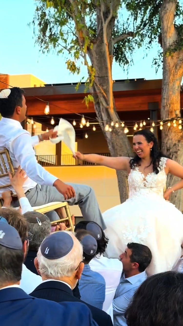 Bride and groom lifted in chairs holding a cloth during a Jewish wedding dance