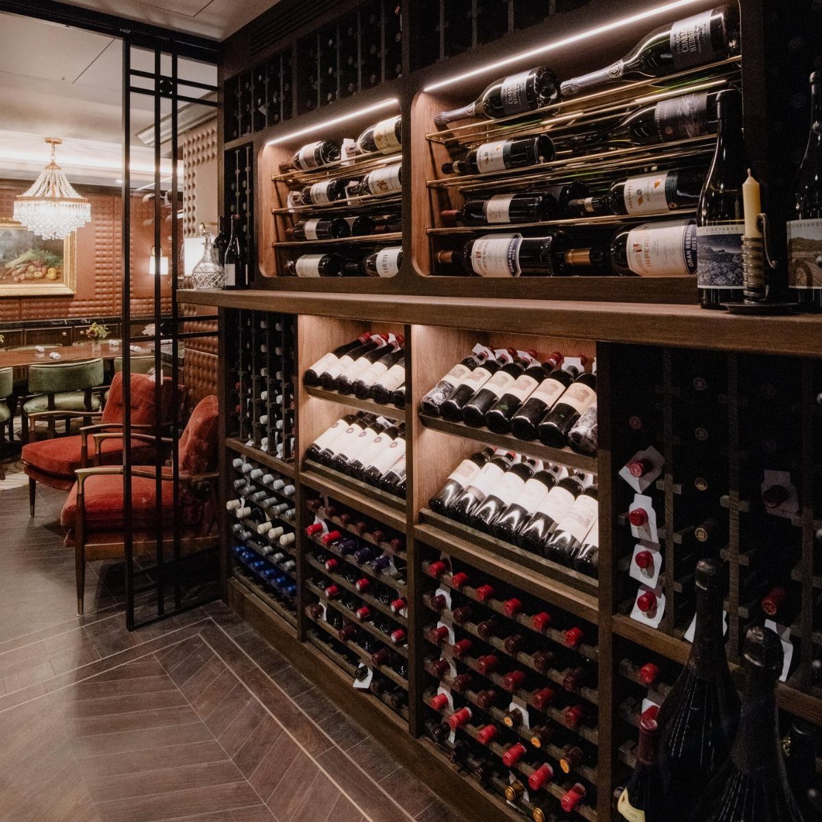 Wine cellar with dark wood racks, red velvet chairs, and herringbone floors.