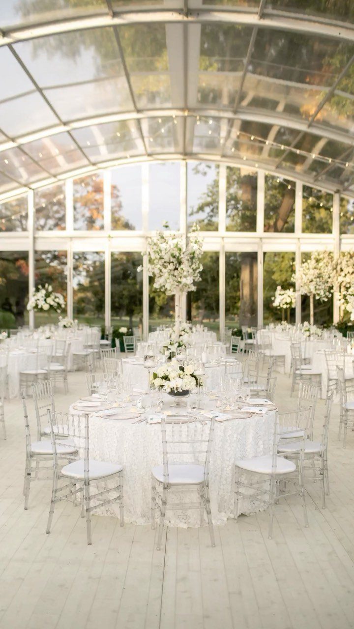 Wedding reception tables with white linens and flowers inside a glass pavilion