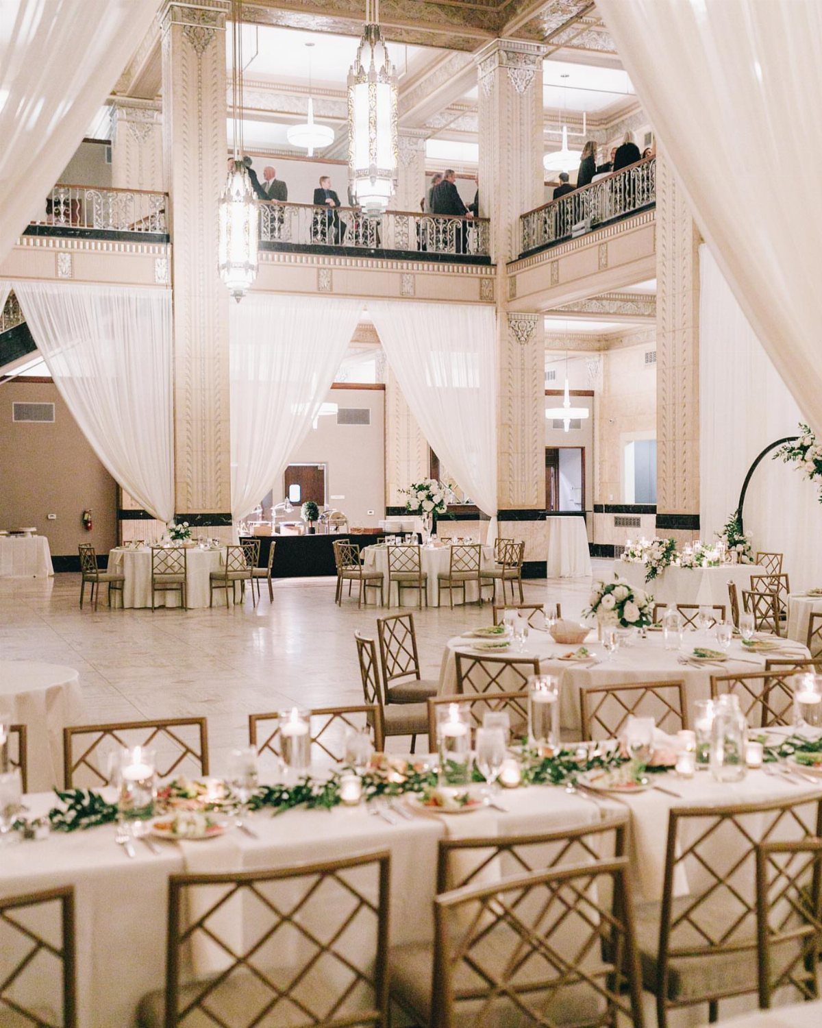 Grand ballroom wedding reception with white drapery, gold chairs, and elegant table settings.