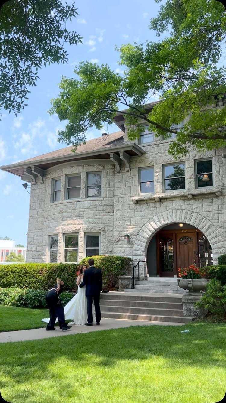 Bride and groom standing in front of a historic stone mansion with green lawns.