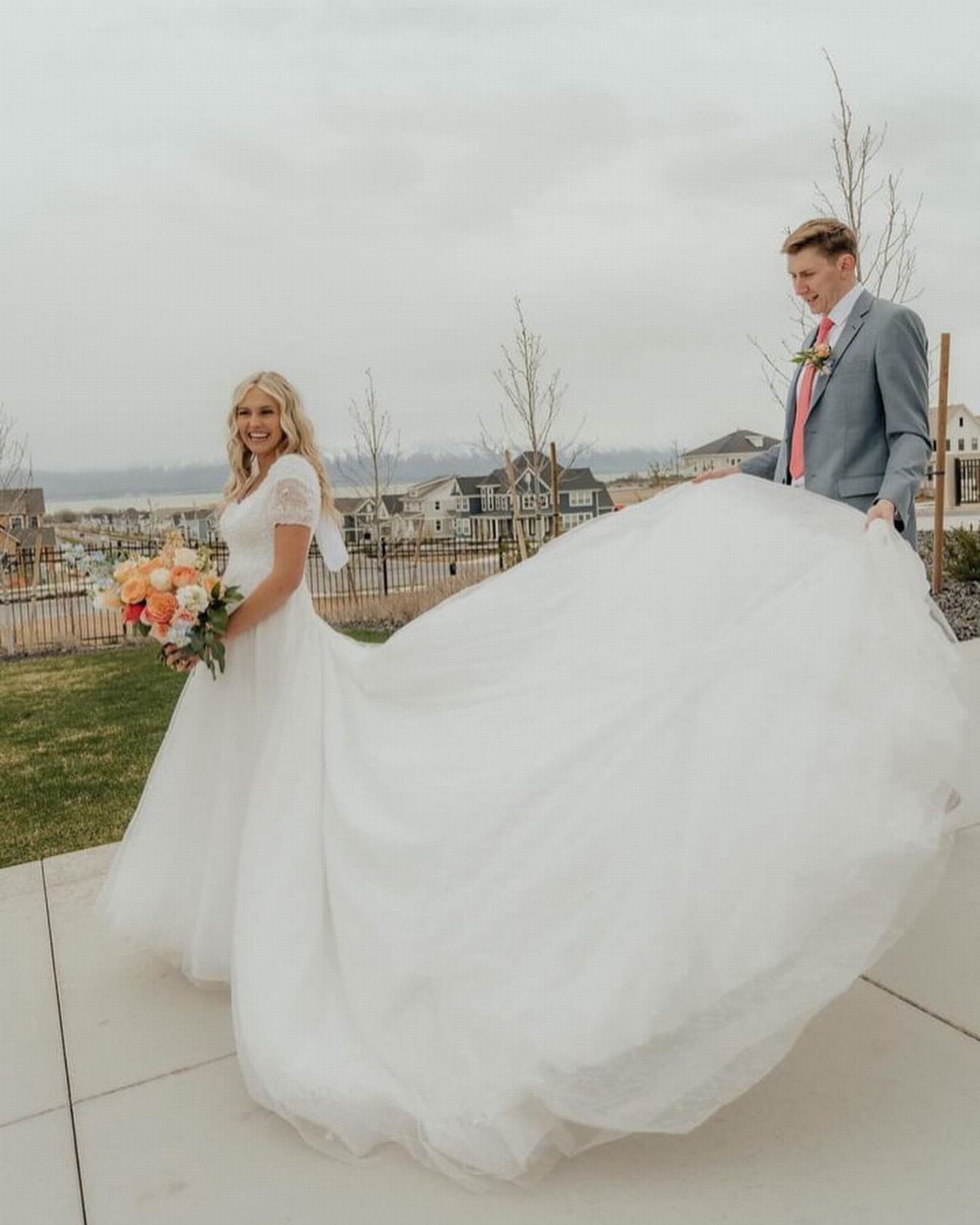Bride in modest white wedding dress and groom in grey suit outdoors.