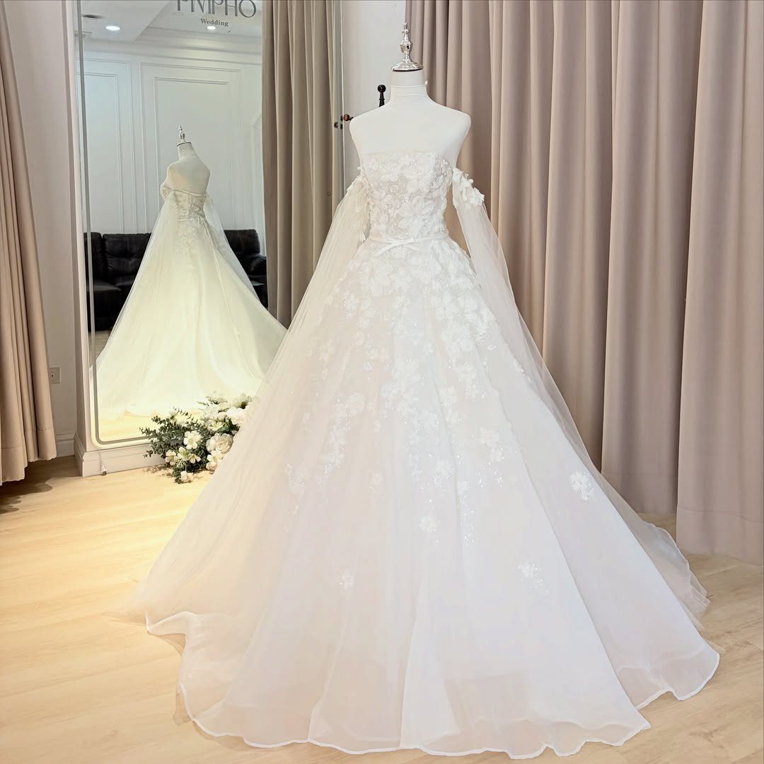 Strapless white wedding gown with floral lace and detachable sheer off-the-shoulder sleeves.
