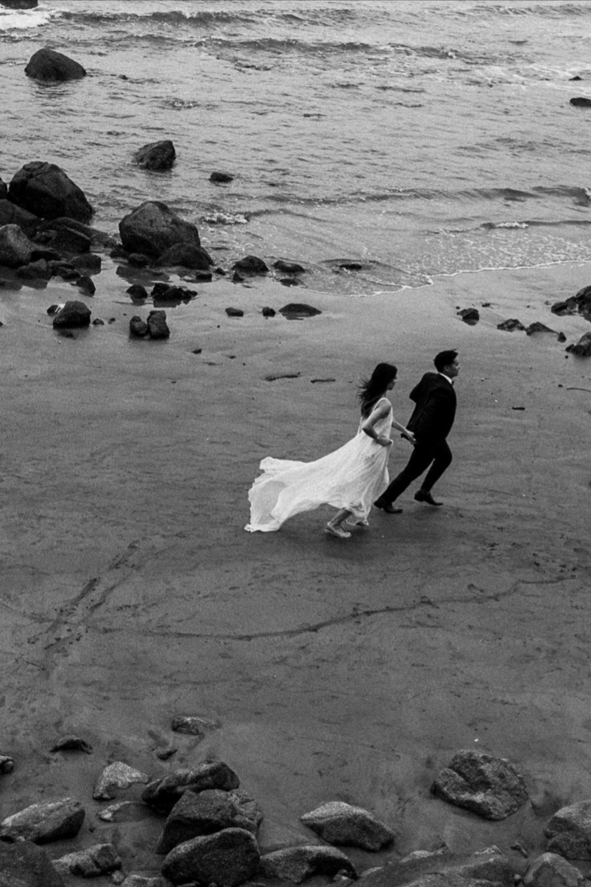 Bride and groom walking on a rocky beach in a black and white photograph
