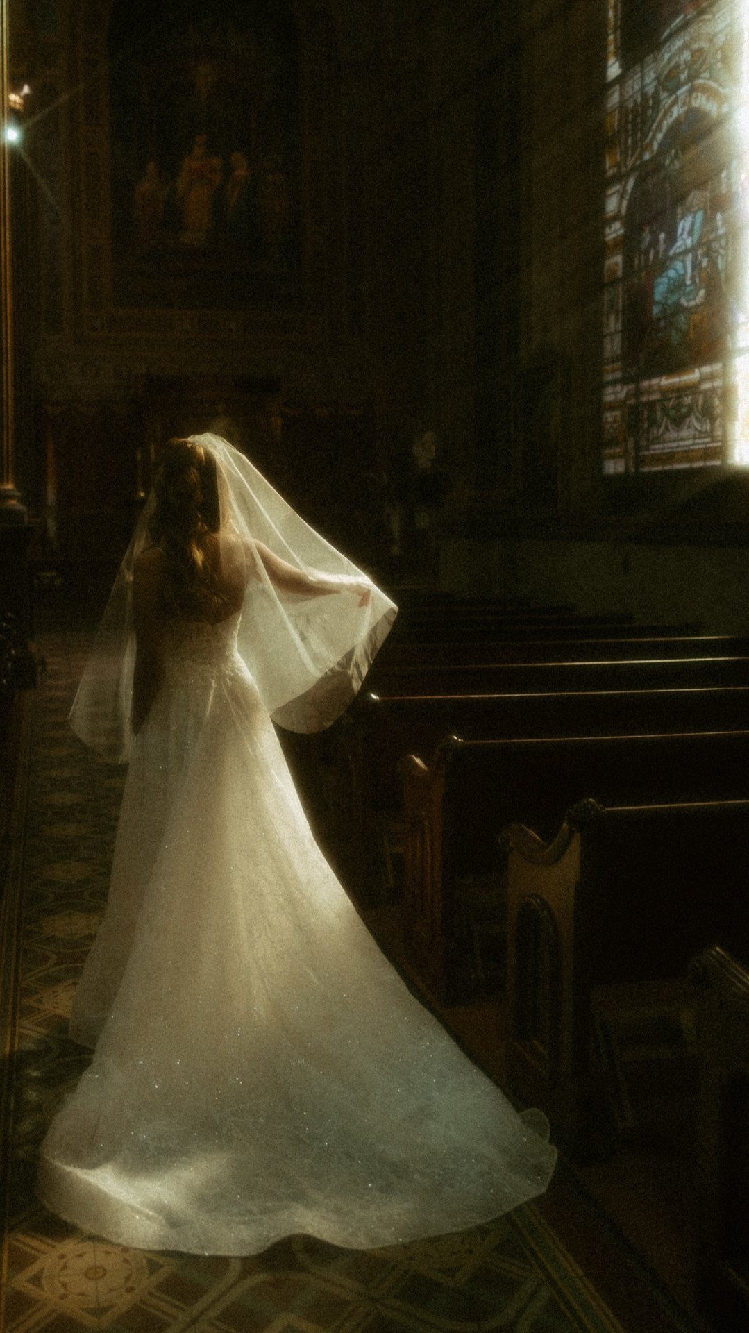 Bride in white dress standing in a dark church with dramatic lighting.