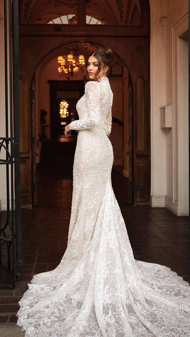 Woman in a white lace long-sleeve wedding dress standing in a stone doorway.