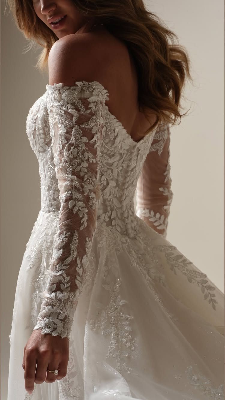 Woman in a white off-the-shoulder wedding dress with long floral lace sleeves.