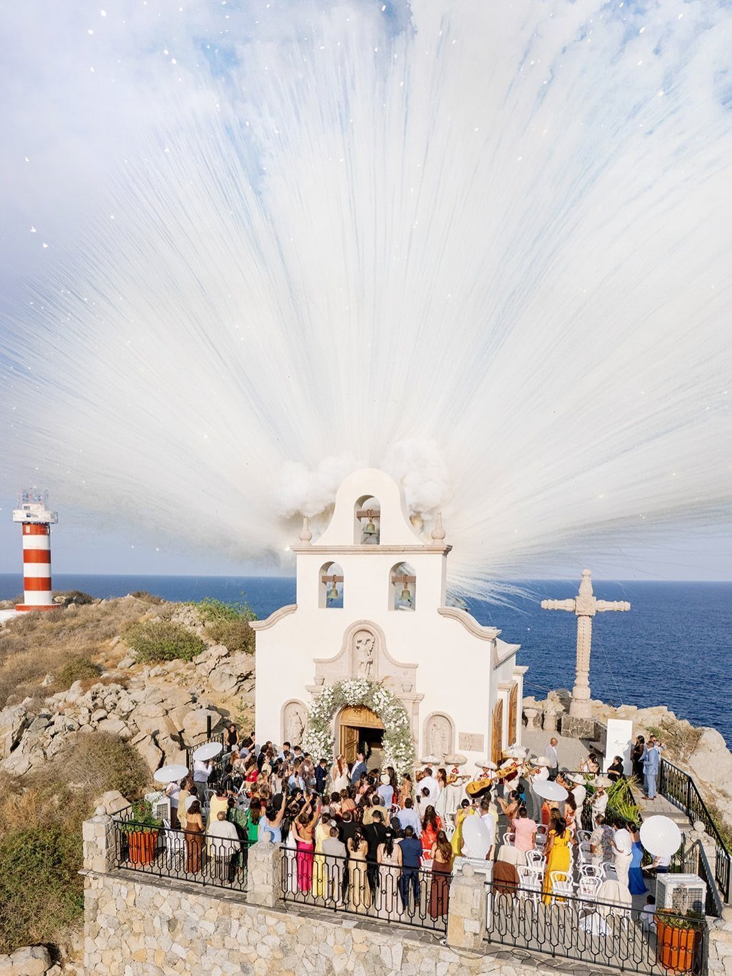 White chapel on a cliff with wedding guests and a large white firework burst.