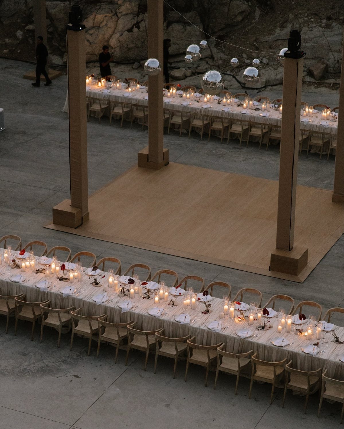 Outdoor wedding reception setup with long candlelit tables and a dance floor by cliffs