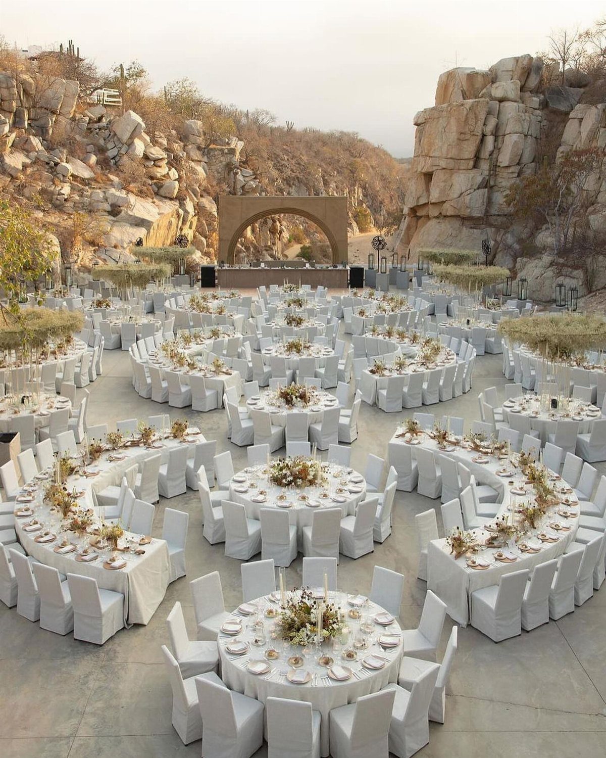 Outdoor wedding reception with white tables and chairs set in a rocky desert canyon.