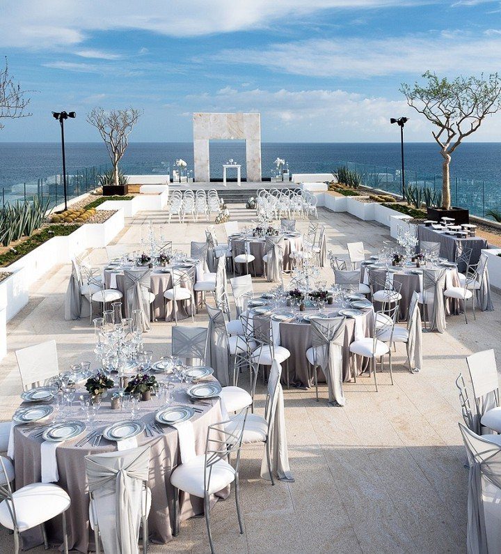 Outdoor wedding reception on a white terrace overlooking the blue ocean with ceremonial arch.