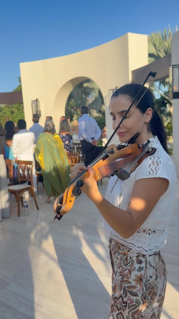 Woman playing violin at an outdoor event with guests seated in the background.