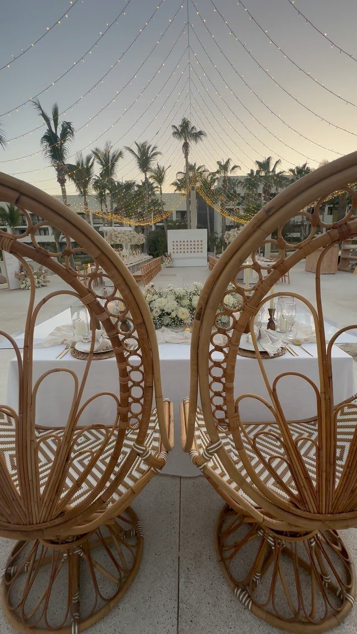 Two rattan peacock chairs at a decorated wedding table with palm trees background