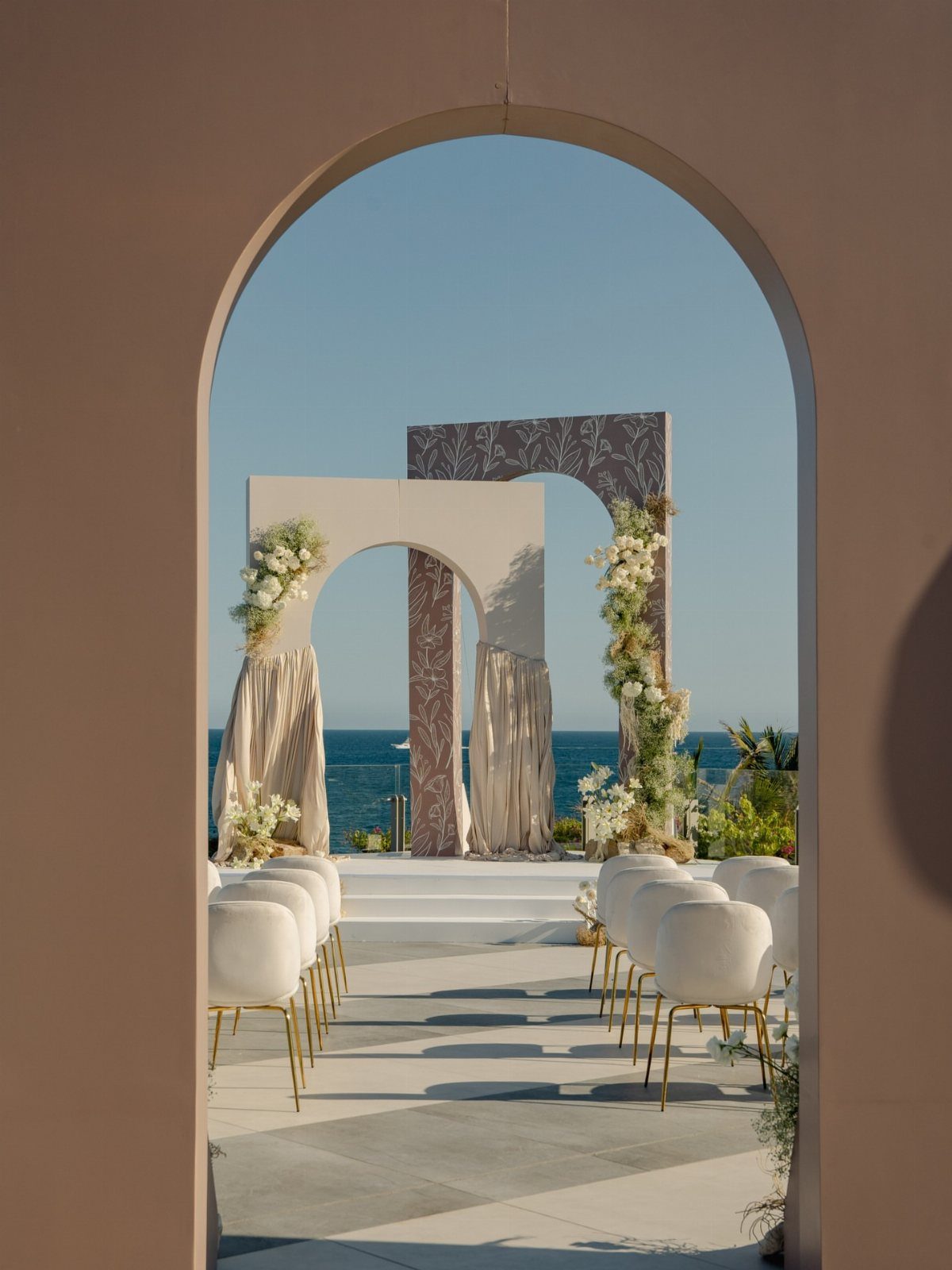 Wedding ceremony setup with white chairs and floral arches overlooking the blue ocean.