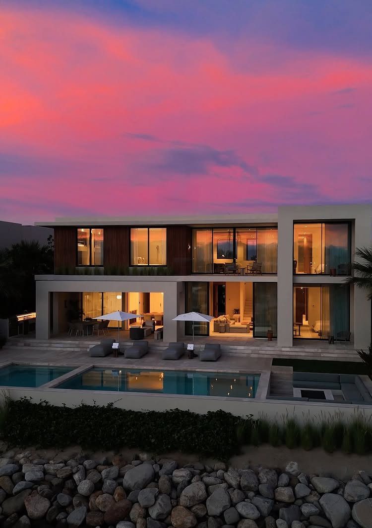 Modern luxury villa with a swimming pool under a pink sunset sky.