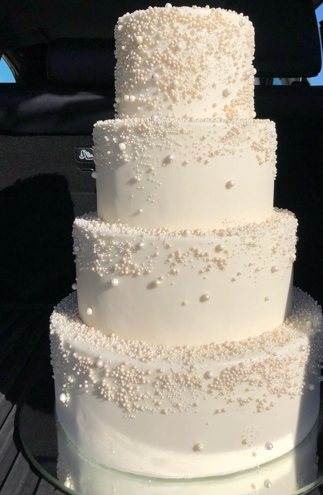 Four-tier white wedding cake decorated with delicate white edible pearls and beads.