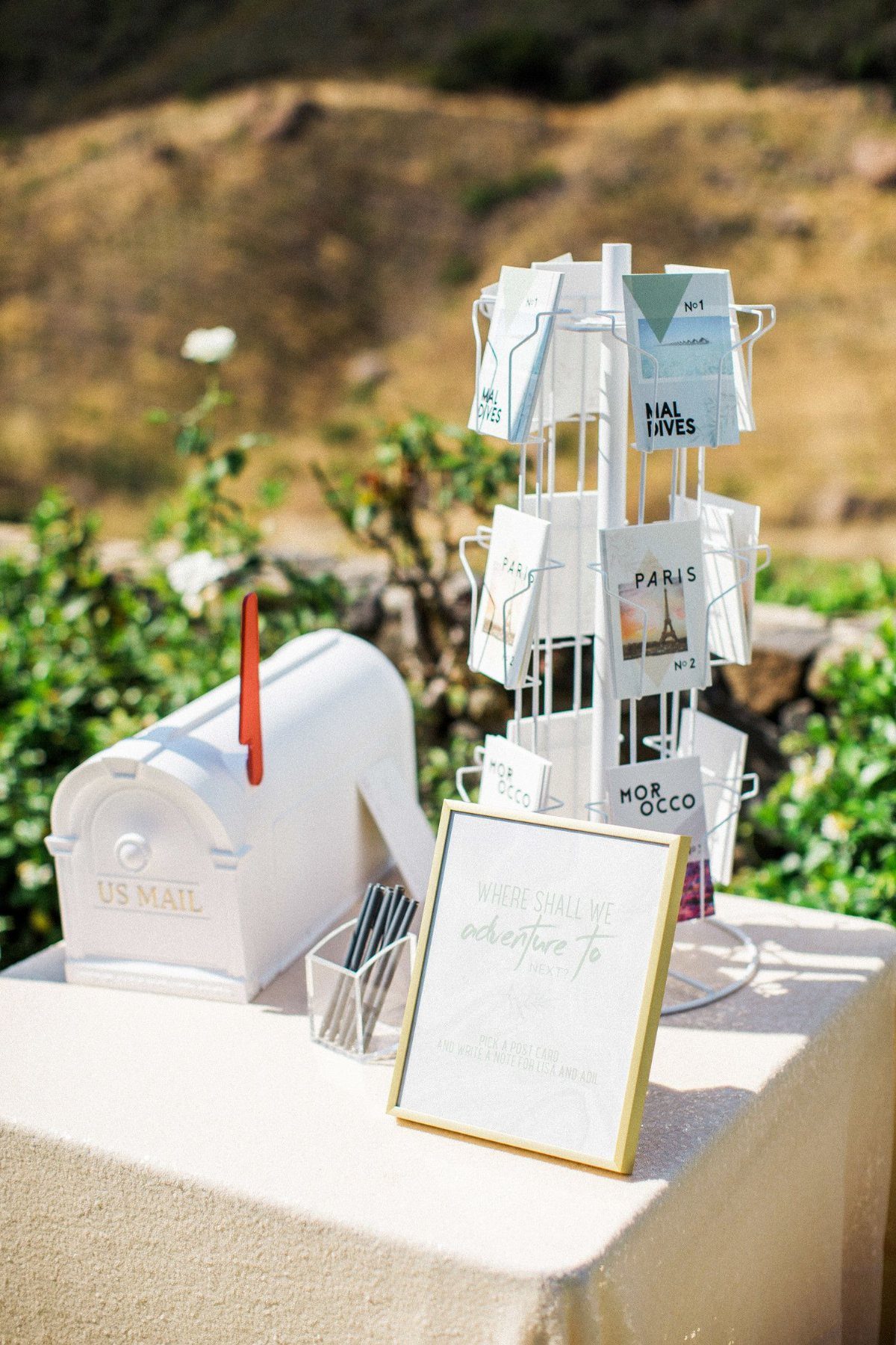 White US Mail mailbox and travel-themed escort card holder on a beige table.