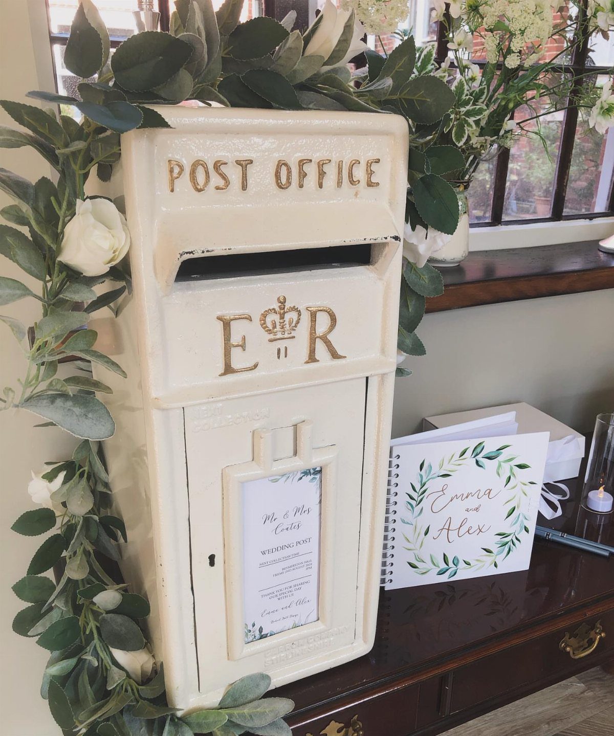 Vintage cream post box decorated with greenery and roses next to a wedding guestbook.