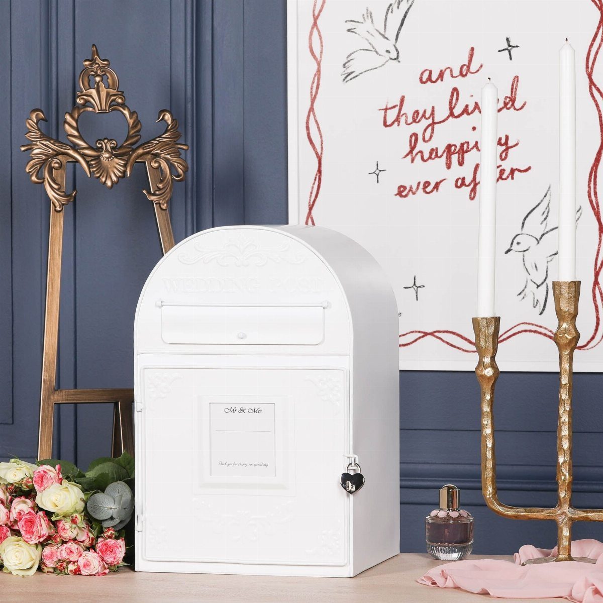 White vintage mailbox with a heart-shaped lock surrounded by roses and candles.