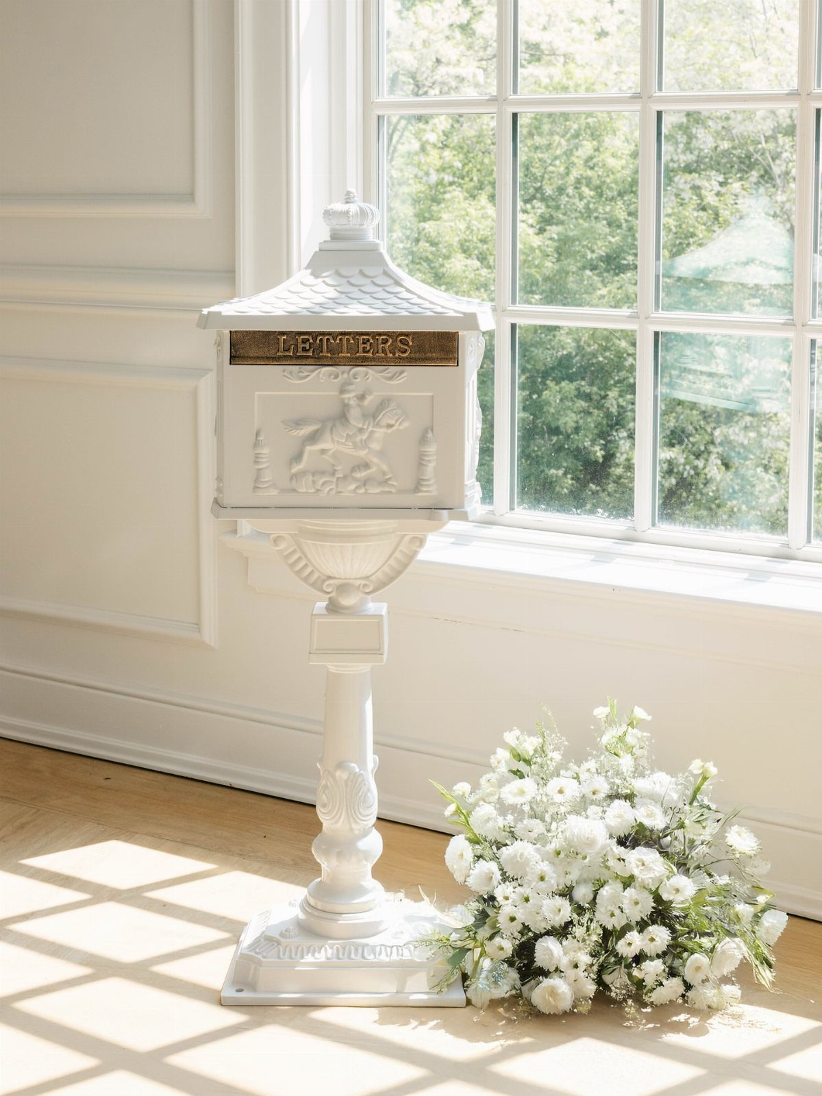 White vintage pedestal mailbox with gold lettering next to white floral bouquet.