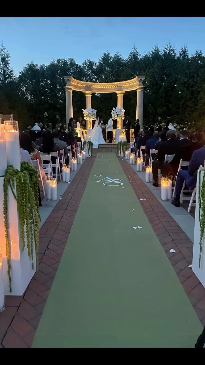 Green aisle runner with white monogram leading to a wedding altar at dusk.