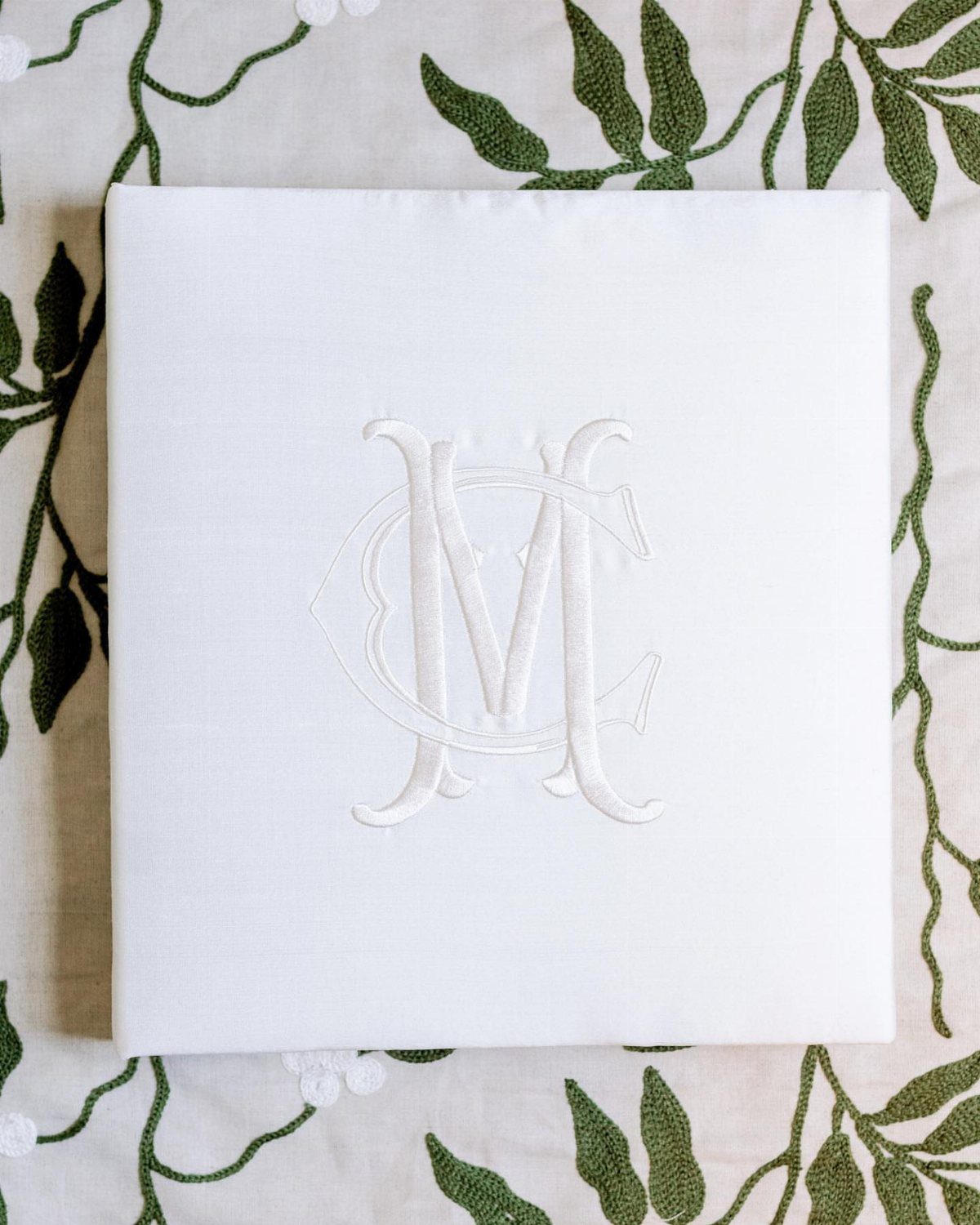 White fabric book with an embossed monogram M on a leaf-embroidered cloth.