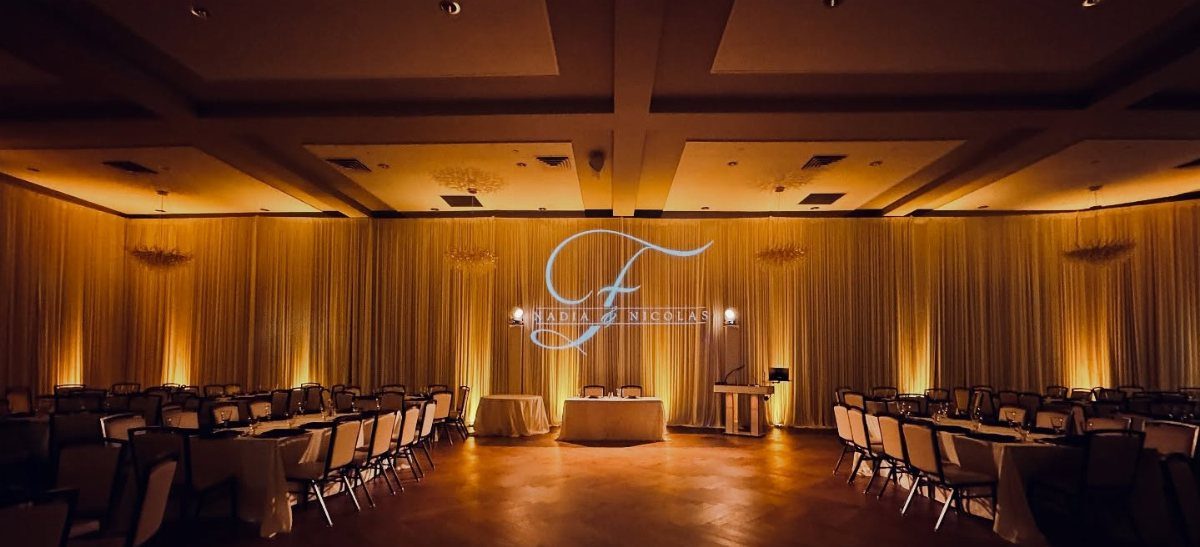 Glowing white monogram F projected onto gold curtains in a wedding ballroom
