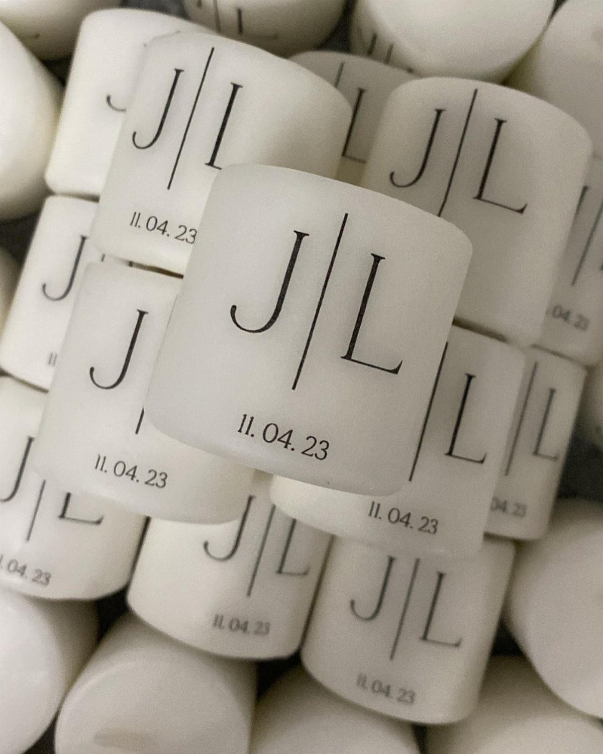 White cylindrical candles featuring a black J L monogram and a wedding date.