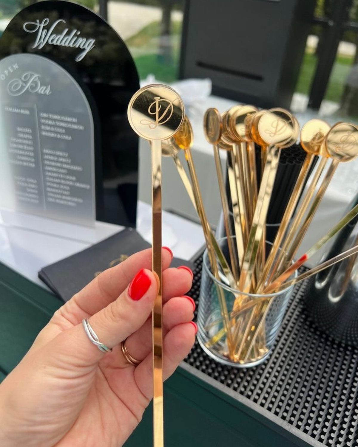 Gold monogrammed drink stirrers held by a hand at a wedding bar