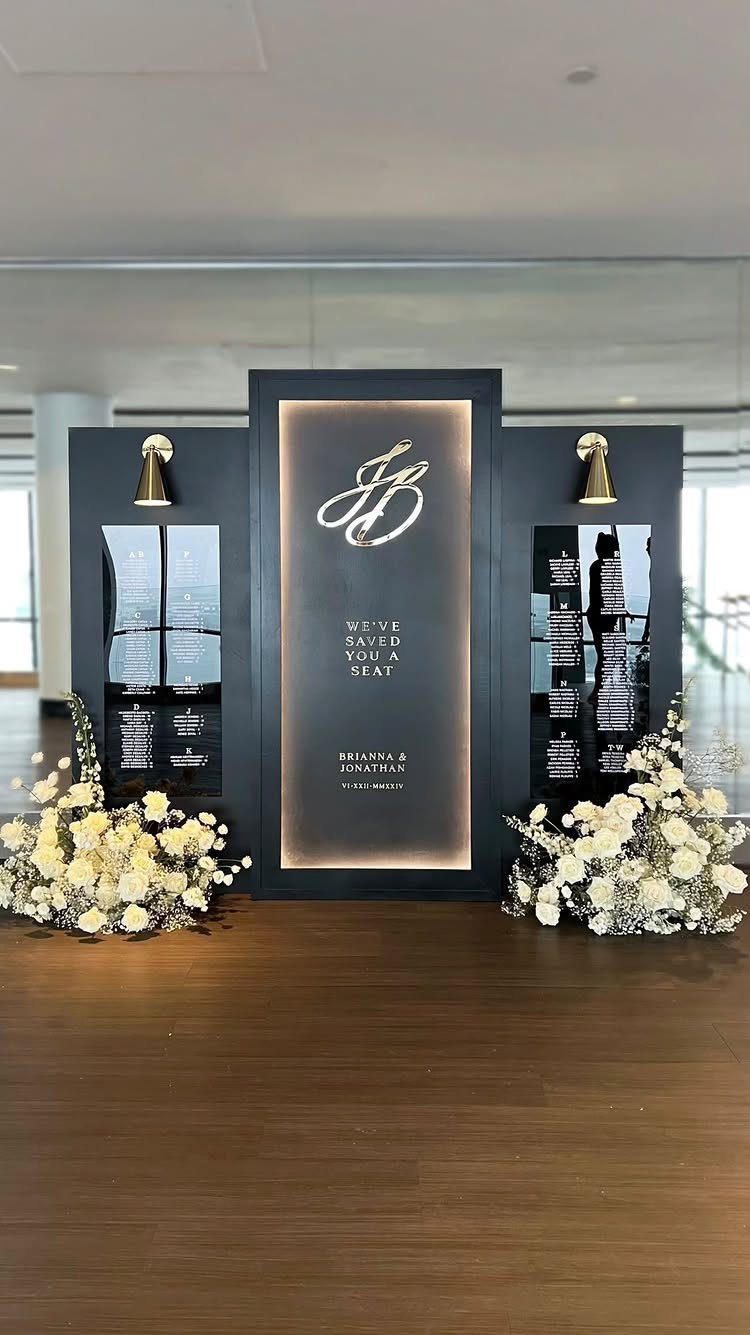 Black wedding seating chart display with gold monogram and white floral arrangements