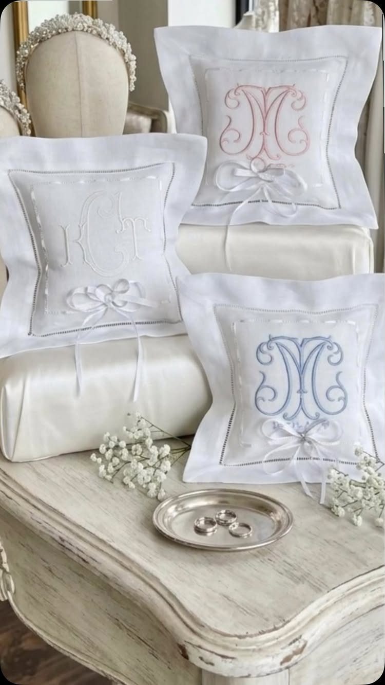 Three white monogrammed ring pillows on a vintage table with wedding rings.