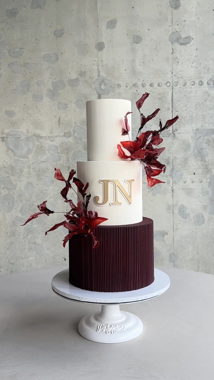 Three-tier wedding cake with gold JN monogram and deep red leaf decorations.