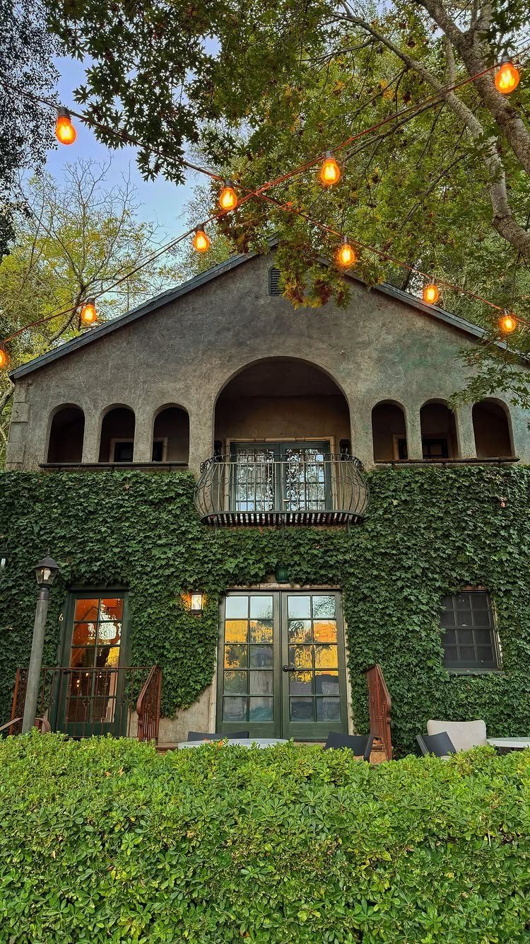 Ivy-covered stone building with arched balconies and glowing orange string lights overhead.