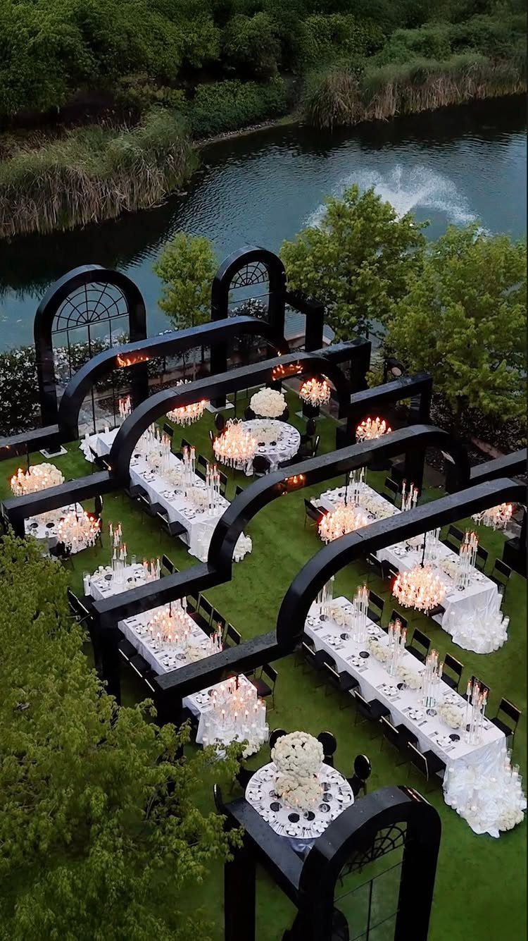 Outdoor wedding reception with white tables and black arches beside a pond fountain.