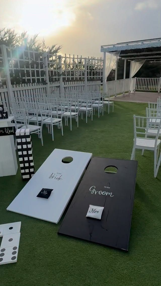 Cornhole boards labeled Bride and Groom on a green lawn with white wedding chairs.
