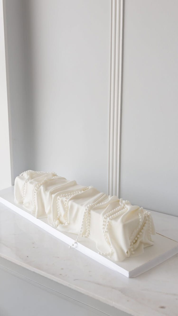 White rectangular wedding cake with draped frosting and pearl beads on marble surface
