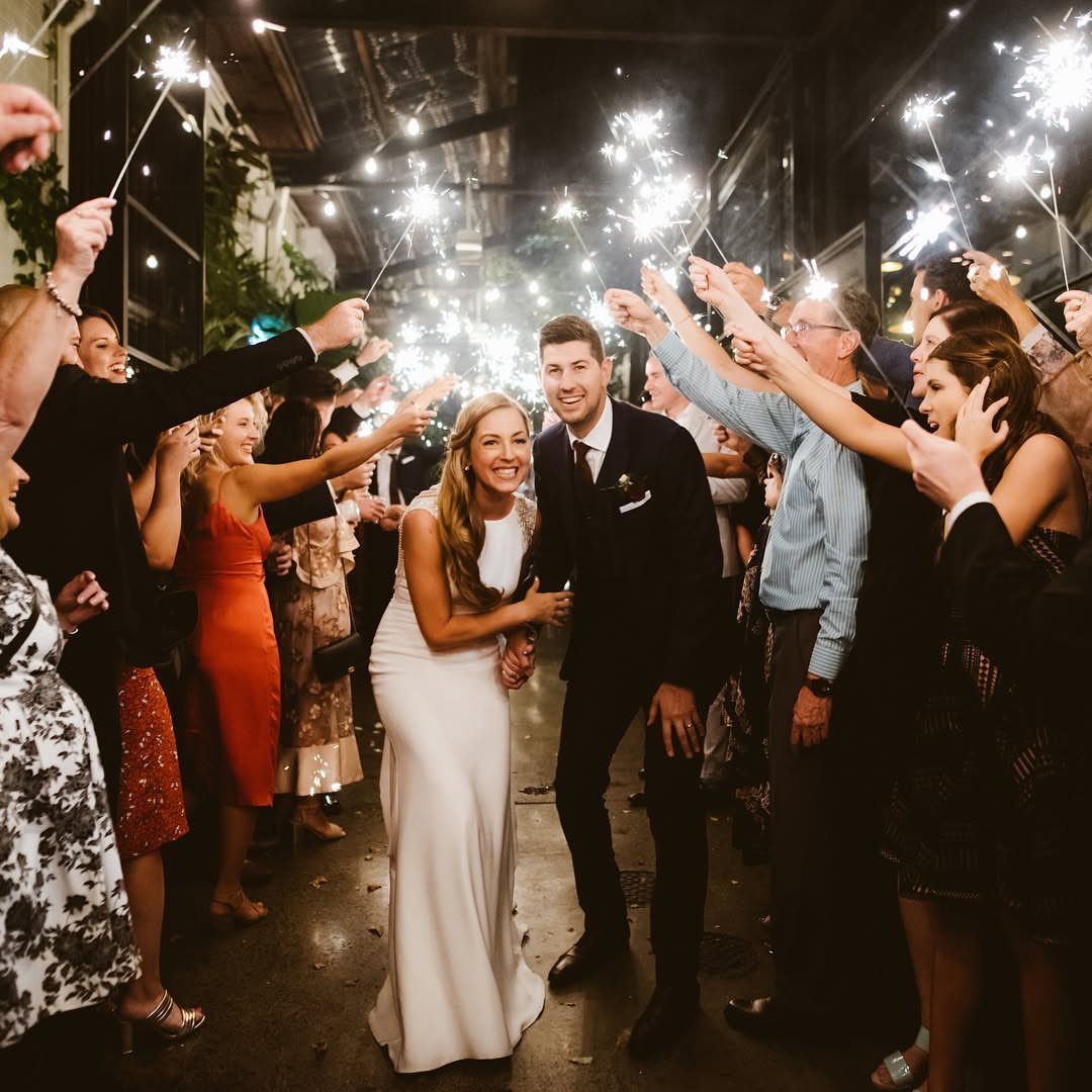 Bride and groom walking through a tunnel of guests holding lit sparklers