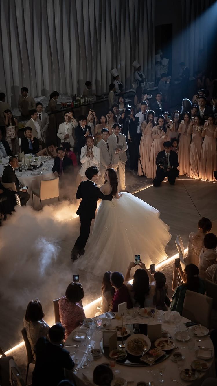Bride and groom dancing in a ballroom with low-lying fog and spotlights.