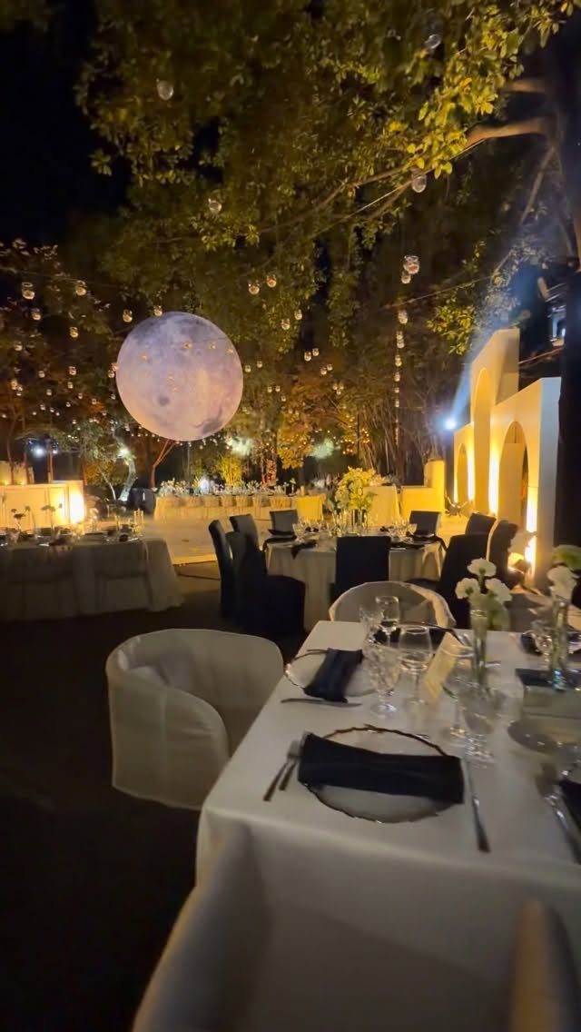 Outdoor evening wedding reception with white tables and a large glowing moon lamp.