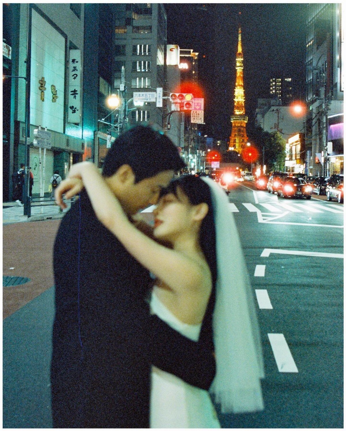 Wedding couple embracing on a city street at night with Tokyo Tower behind them