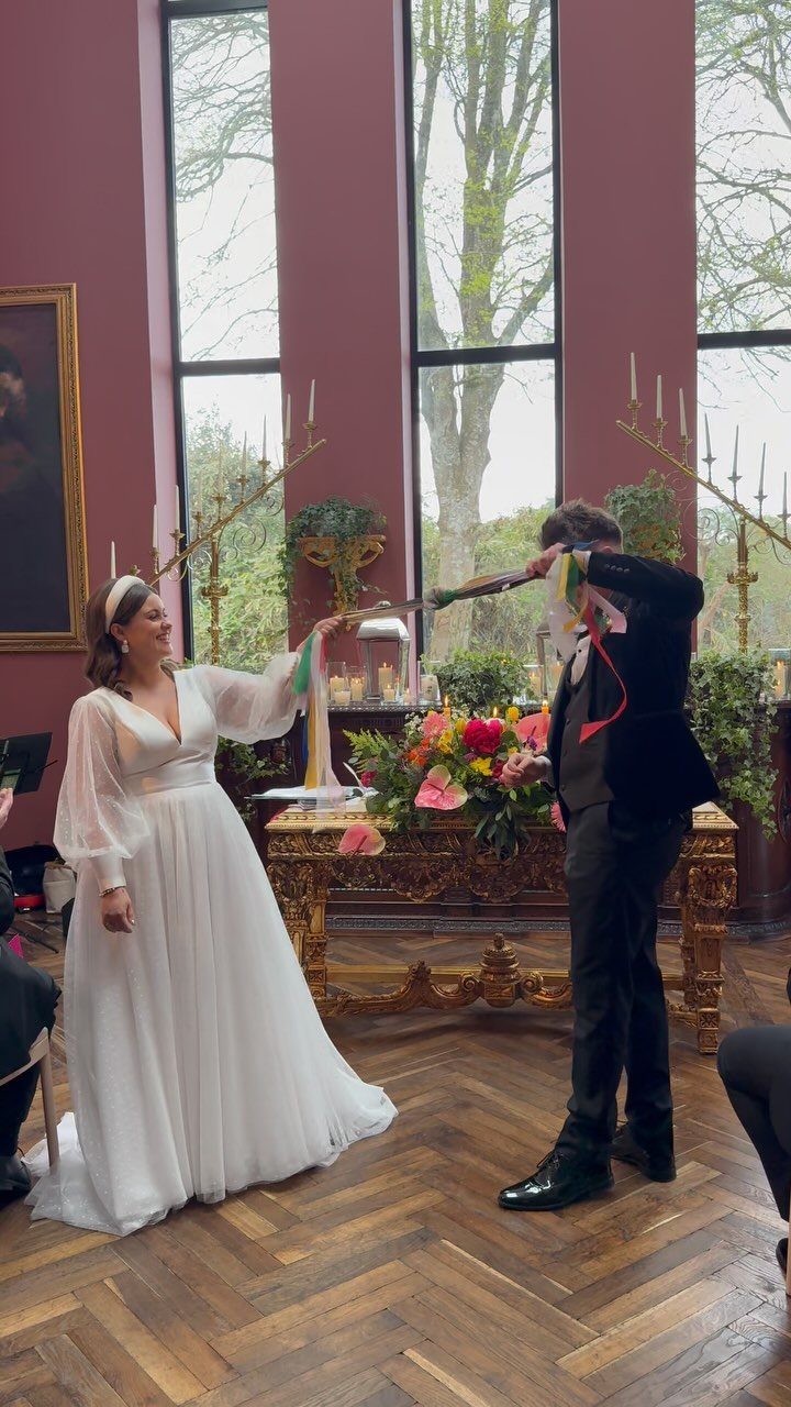 Bride and groom holding a colorful ribbon during a handfasting wedding ceremony.
