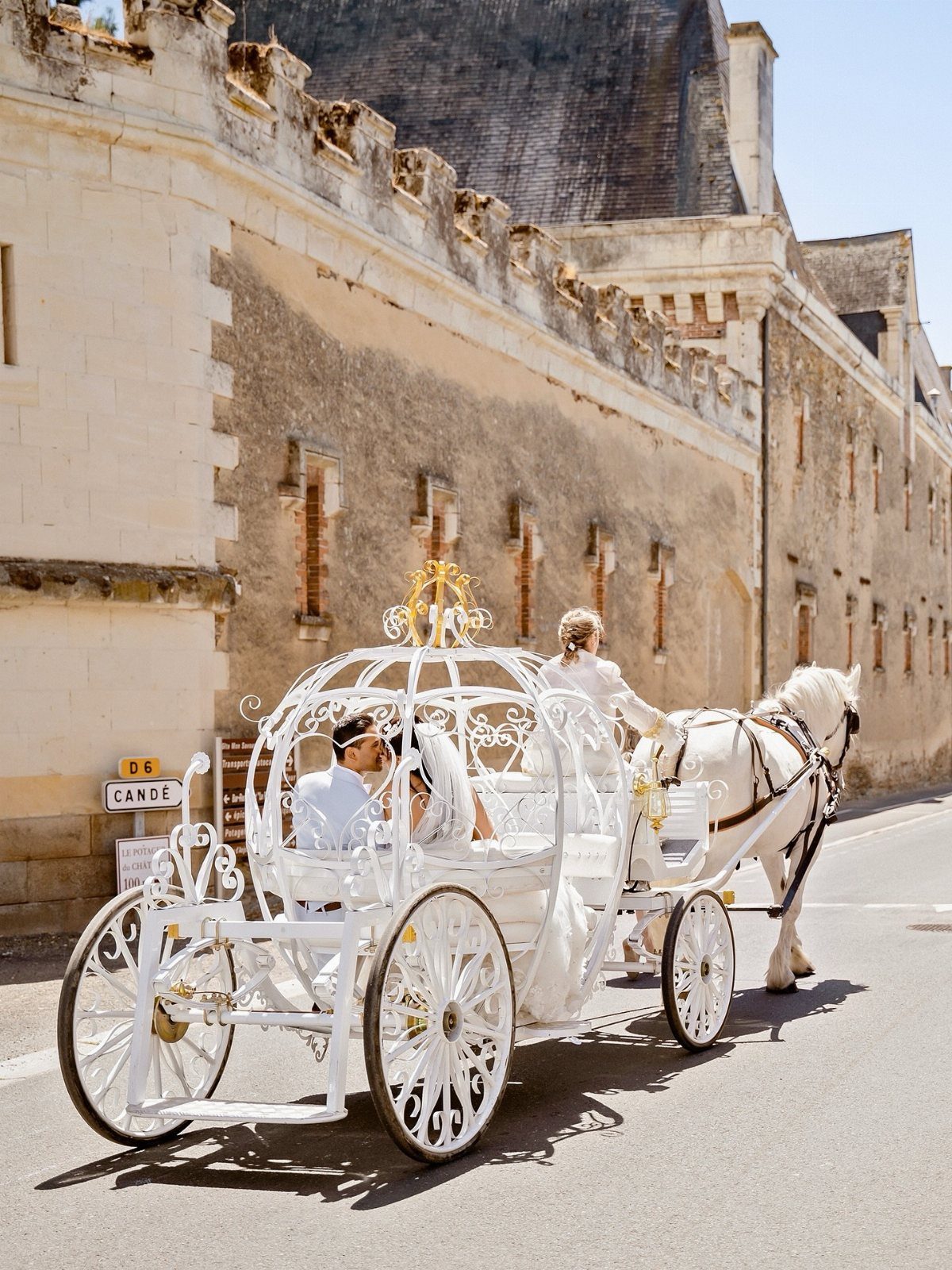 Couple in wedding attire kissing in an ornate white horse-drawn carriage on a road