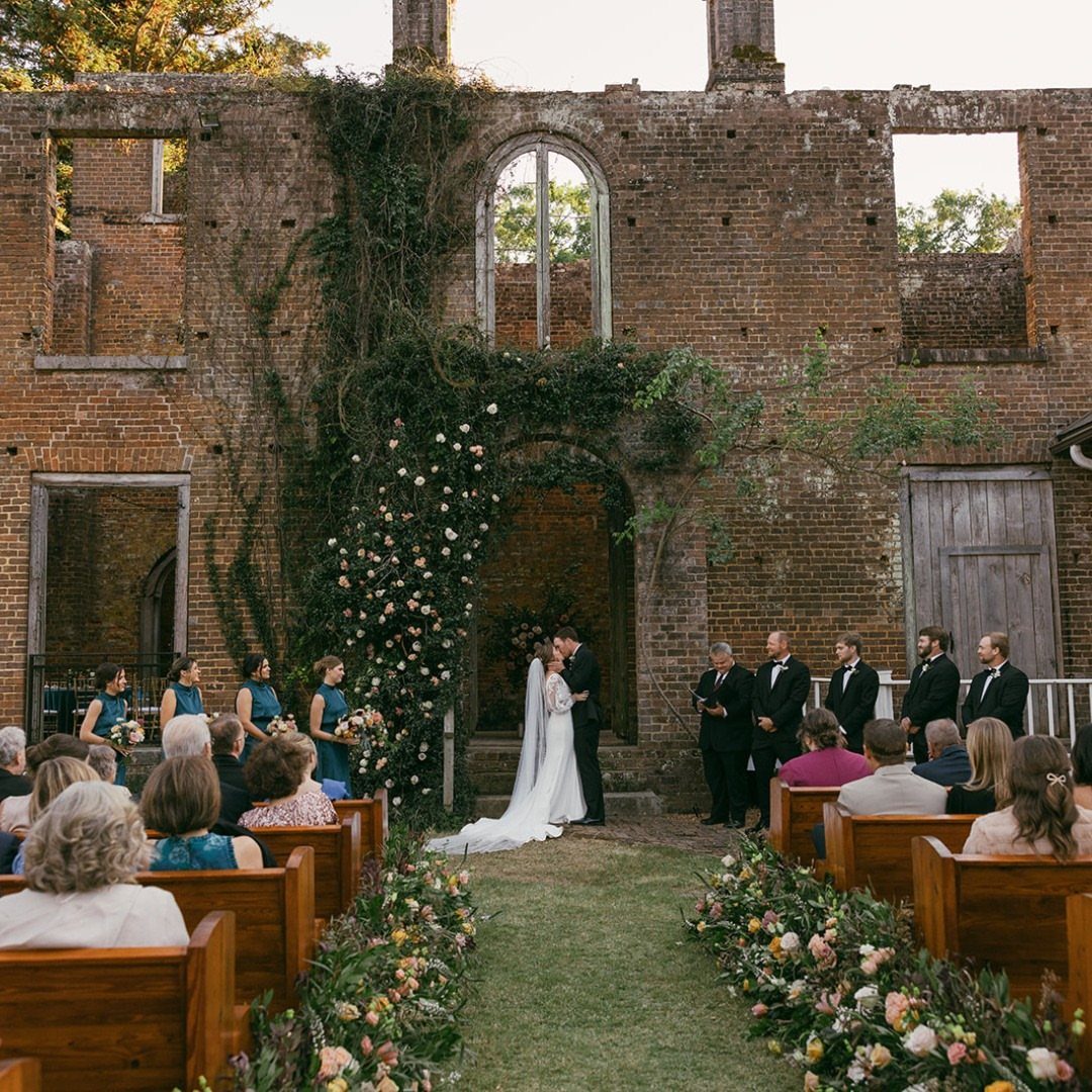 Wedding ceremony in brick ruins with floral arch and guests in wooden pews