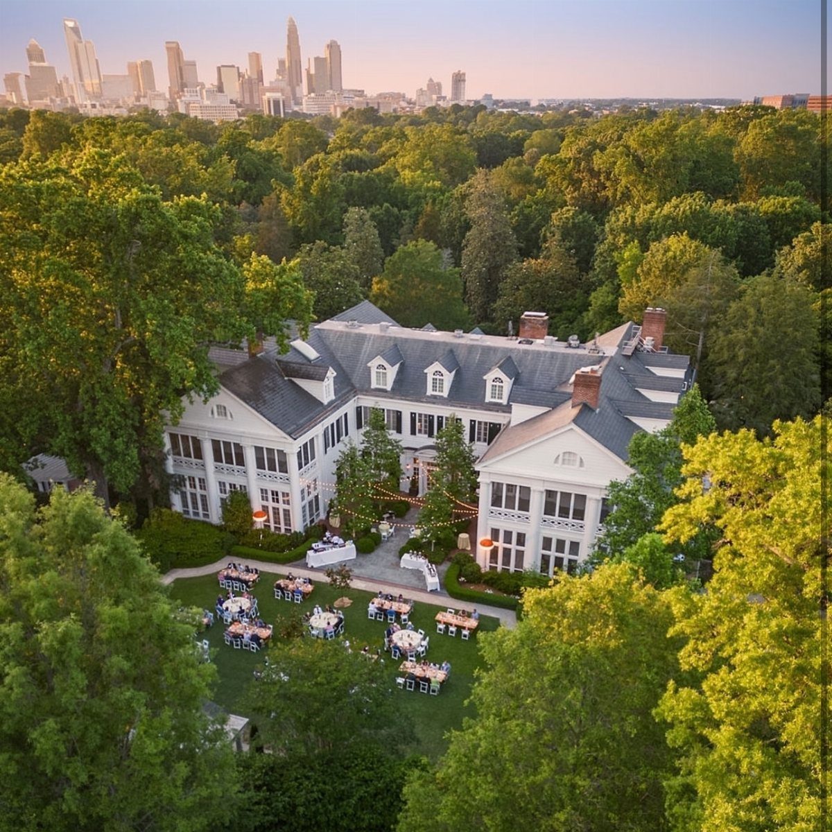 Large white luxury estate with outdoor dining tables set on a green lawn.