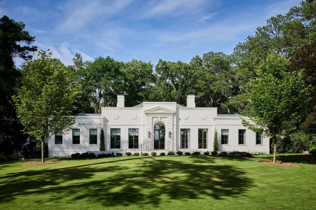 White neoclassical mansion with symmetrical architecture and green lawn under blue sky