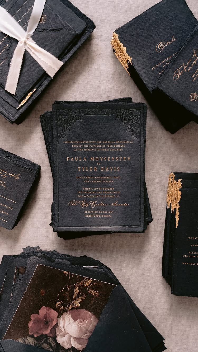 Dark navy wedding invitations with gold calligraphy and white ribbons on neutral fabric.