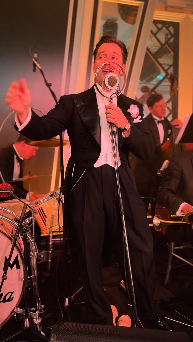 Male singer in a tuxedo performing with a vintage microphone and jazz band.
