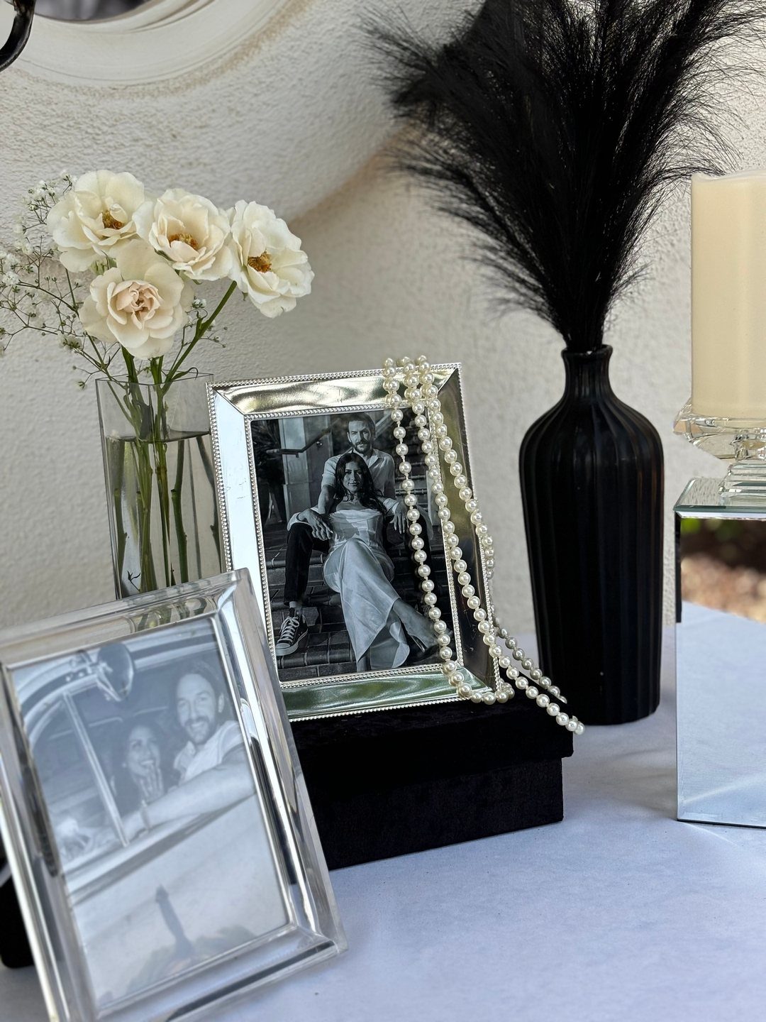 Table display with black and white photos, white roses, pearls, and black feathers.