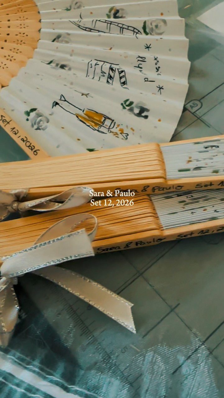 Personalized wedding favors including a decorated folding fan and a ribbon-tied notebook.