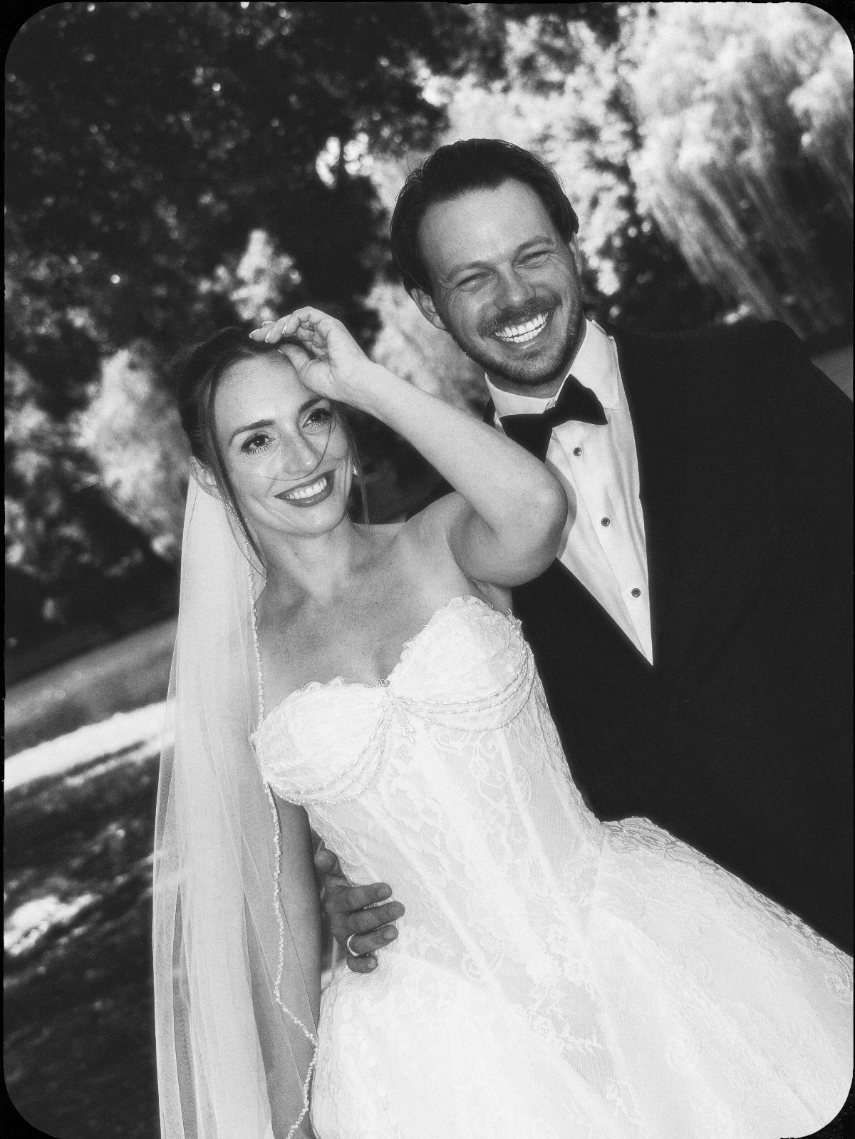 Smiling bride and groom in classic wedding attire in a black and white portrait.